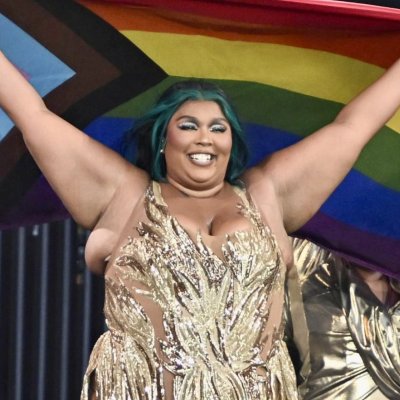 Picture of Lizzo. She is holding a pride flag whilst performing at glastonbury.